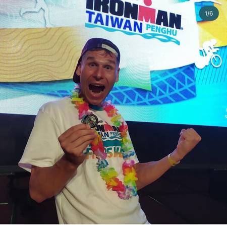 Triathlonista świętuje metę IRONMANA z medalem i kwietnym wieńcem - plan treningowy IRONMAN od IM Inspiration