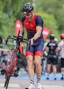 Triathlonista w stroju startowym biegnie z rowerem ze strefy zmian - aplikacja treningowa triathlonu IM Inspiration