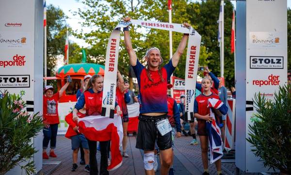 Triathlonista przekracza metę z uniesionymi rękami po zawodach triathlonowych - plan treningowy triathlonowy IM Inspiration