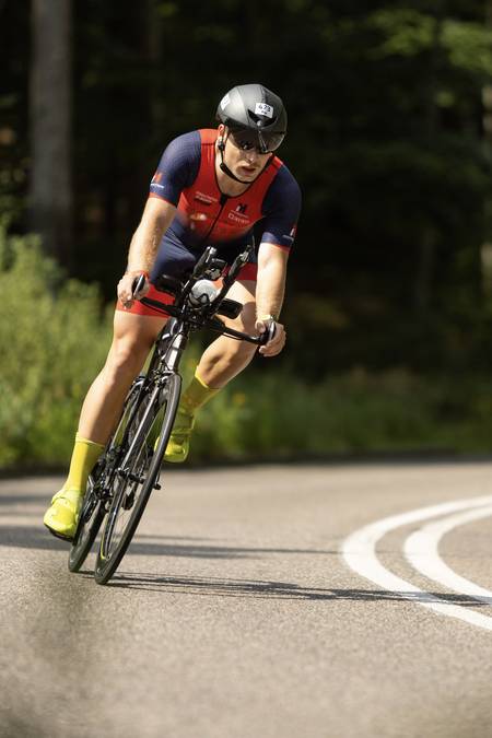 Kolarz w kasku aero wchodzi w zakręt leśnej drogi na rowerze czasowym - plan treningowy kolarski IM Inspiration