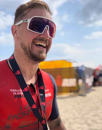 Uśmiechnięty triathlonista na plaży po ukończeniu zawodów triathlonowych - plan treningowy triathlonowy IM Inspiration